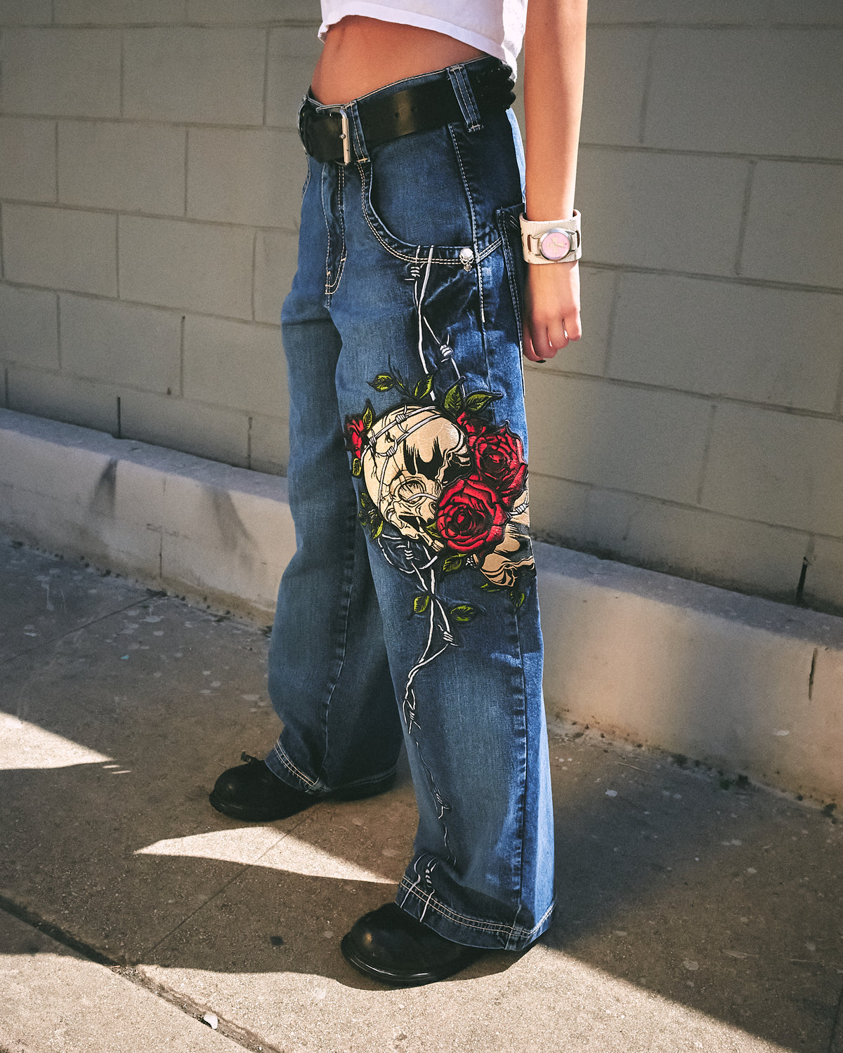 Side view from waist down of the wide-leg jeans showing the skull and red rose embroidery with barbed wire down the leg
