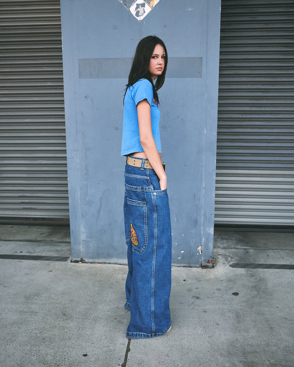 Model wearing dark stone wash wide-leg jeans with a hand in the back pocket, side view showing the Buddha patch