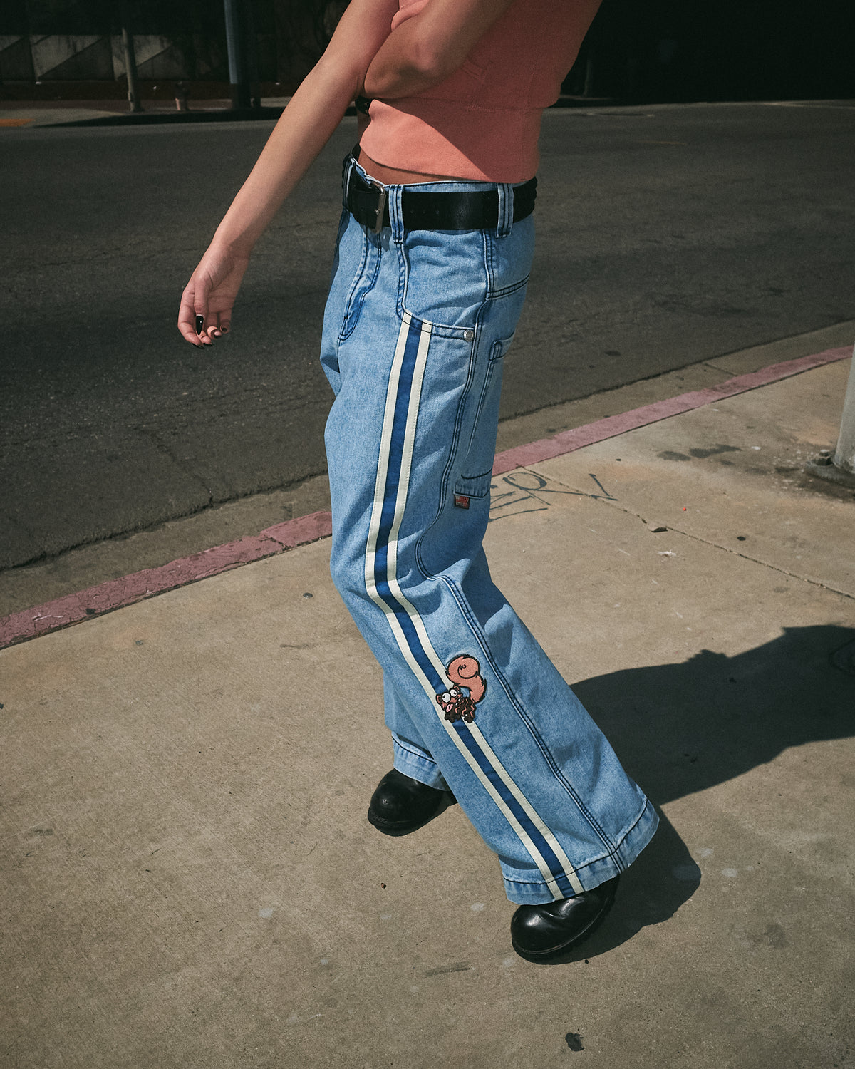 Model walking on a sidewalk in the light-wash wide-leg jeans, side view of the leg tape, squirrel and full-length leg