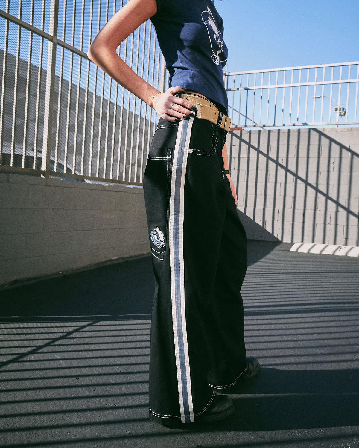 Model wearing black wide-leg jeans, side view showing the striped leg tape and embroidered skunk face