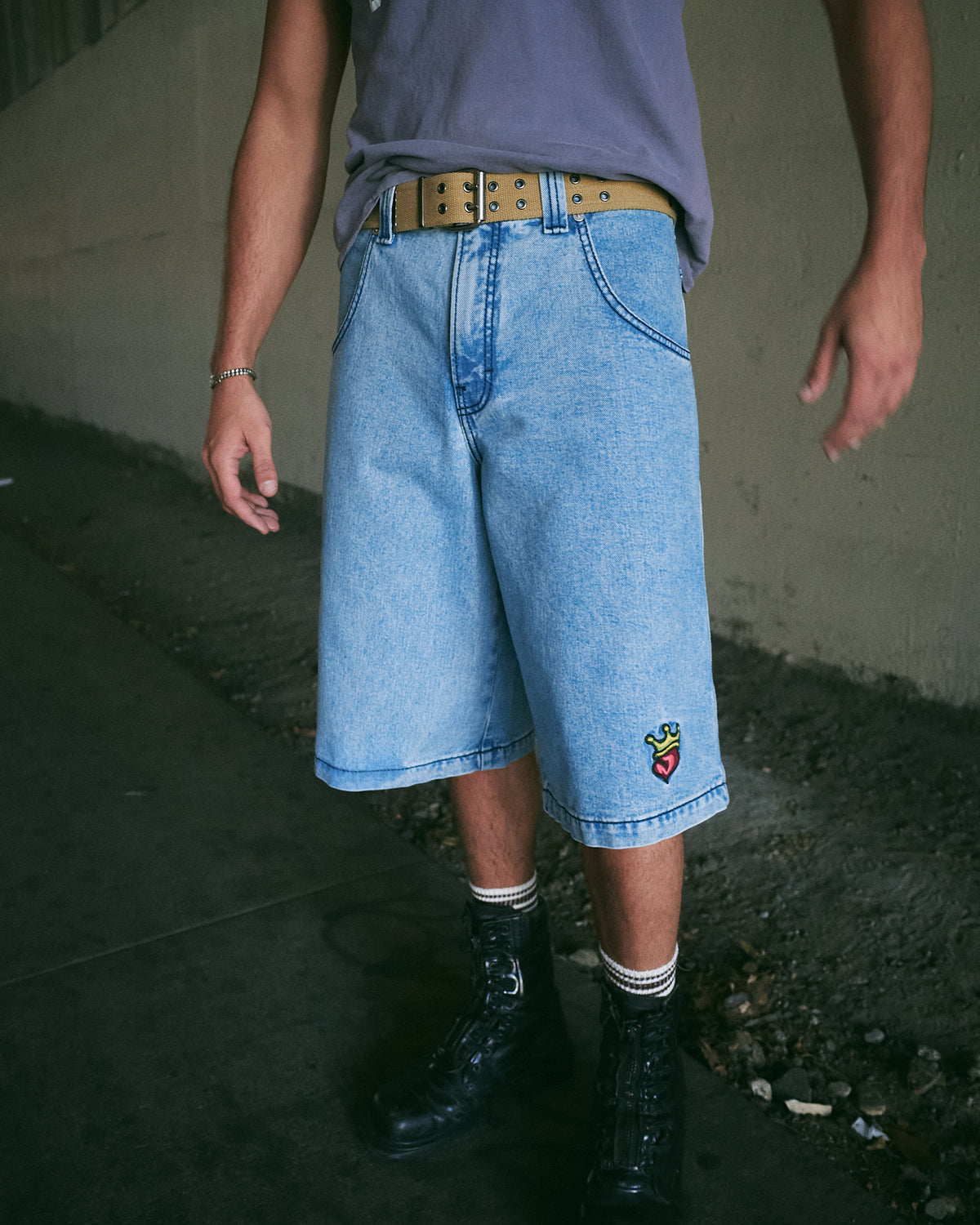 Model wearing light blue wide denim shorts below the knee with an embroidered crowned heart on one leg