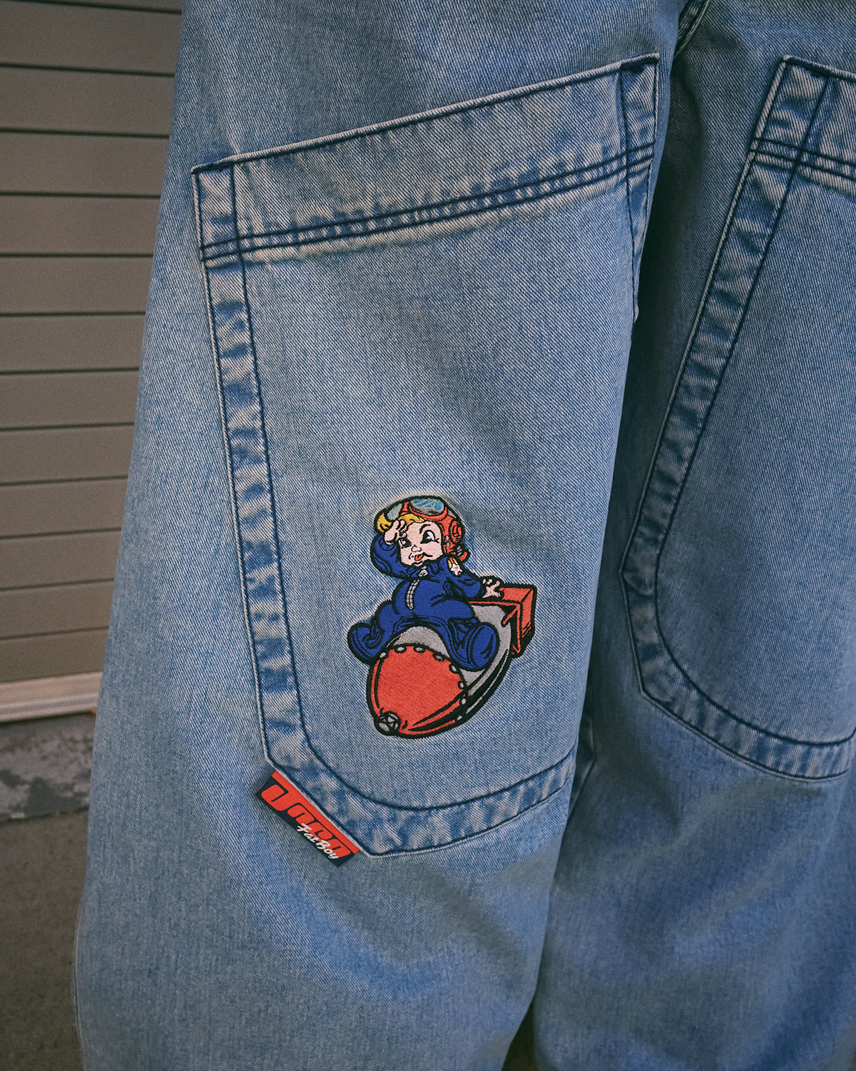 Back pocket embroidery and red JNCO Fat Boy tab on light blue jeans, shown outdoors