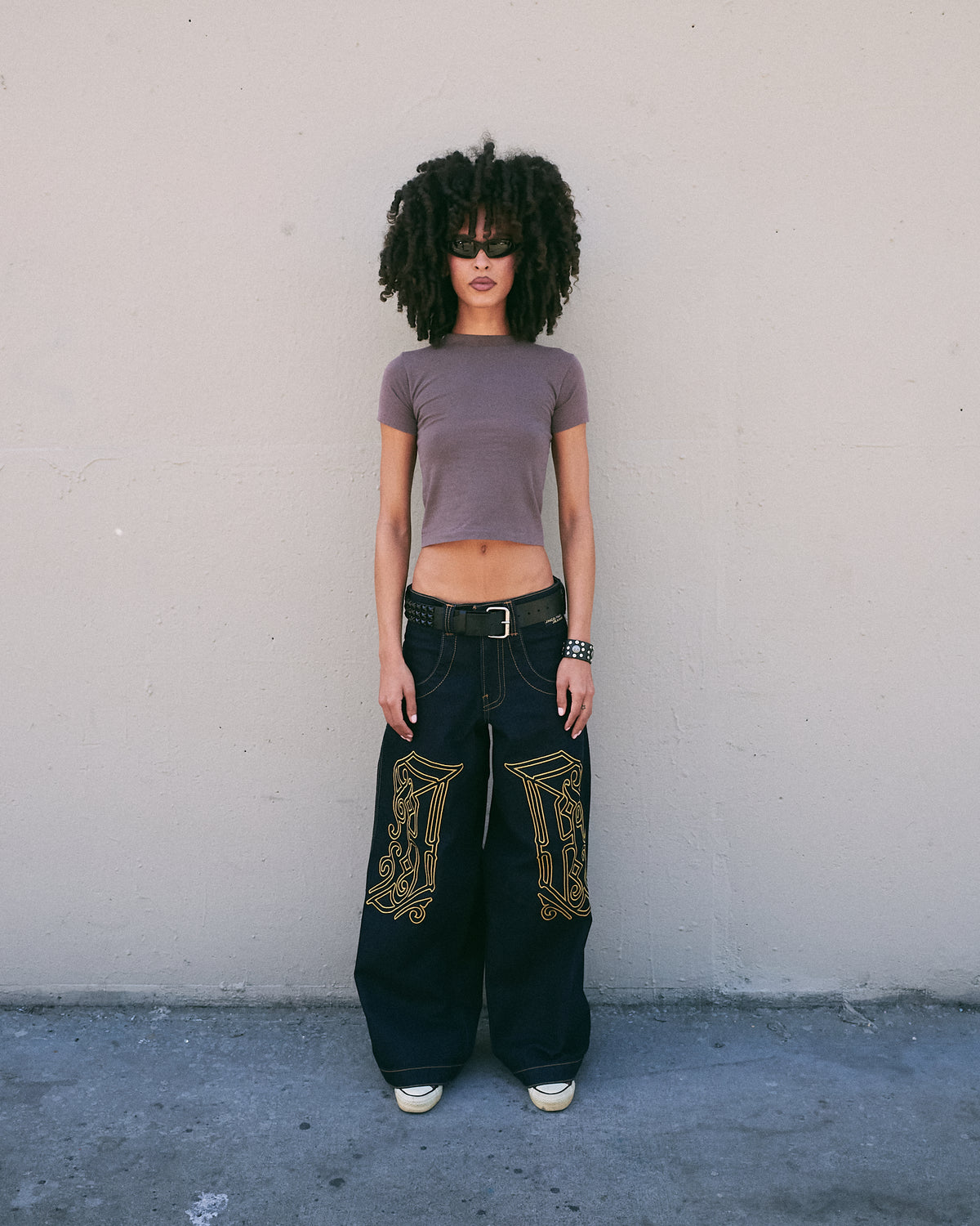Model standing facing forward in very wide-leg dark indigo jeans with gold J monograms on both thighs, full length