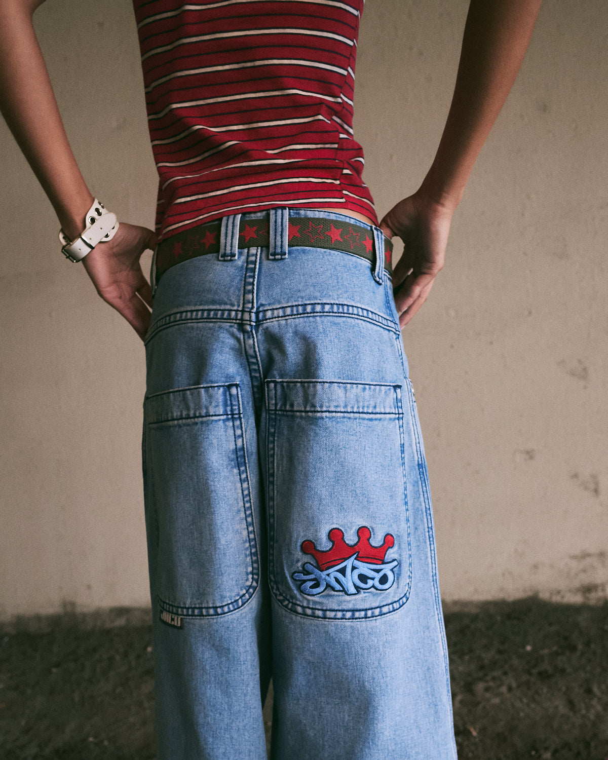 Model with hands on hips wearing light-wash wide-leg jeans, back view showing crown JNCO logo pocket