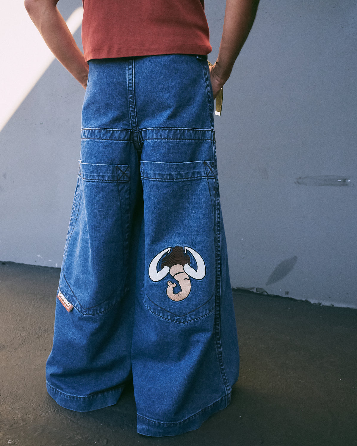 Back of wide-leg dark stone wash jeans from waist to hem, with mammoth embroidery on a back pocket