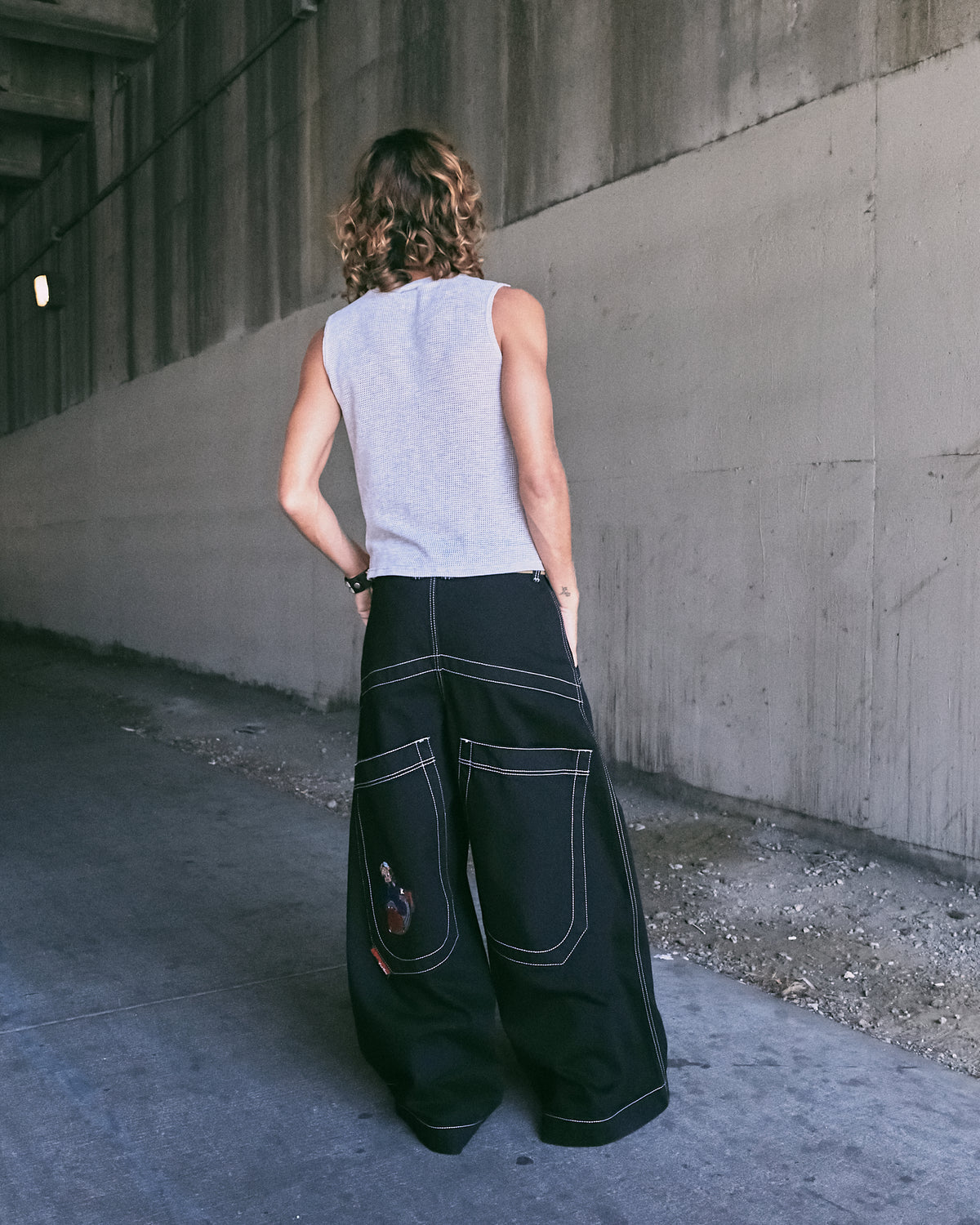 Model wearing extra-wide black jeans, back view showing large back pockets, white stitching and embroidered left pocket