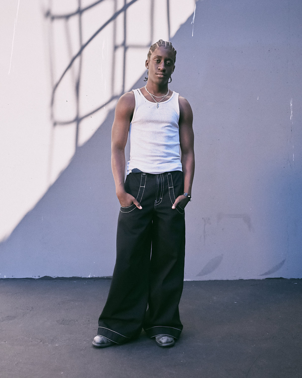 Model wearing black wide-leg jeans with white contrast stitching and a white tank top, full-length front view