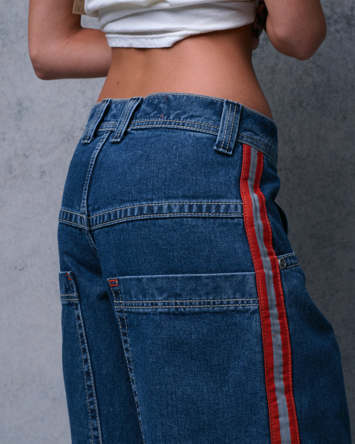 Model wearing low-rise dark stone wash jeans, rear three-quarter view of the waistband, back yoke and side stripe
