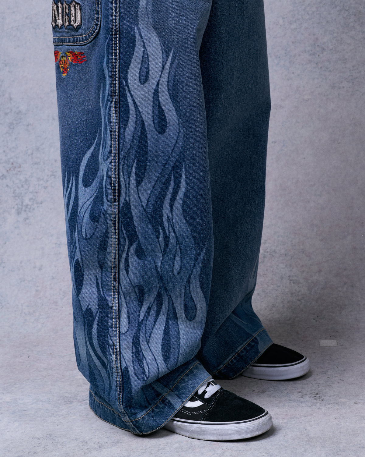 Wide jean leg with tonal flame print from hip to hem, worn over black and white sneakers