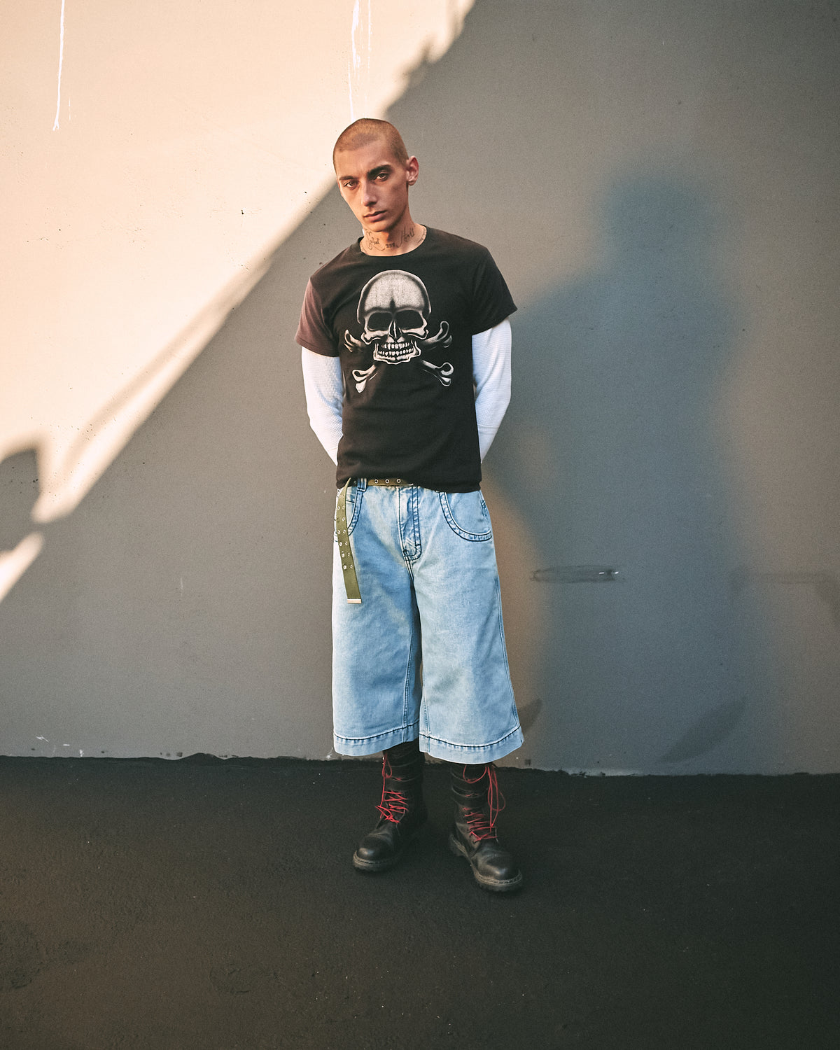 Model standing against a wall in light blue wide denim shorts, skull T-shirt and black boots, front view