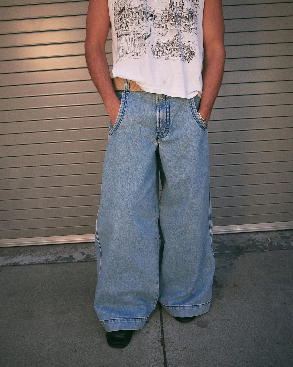 Model standing with hands in the pockets of light blue wide-leg jeans in front of a garage door, front view