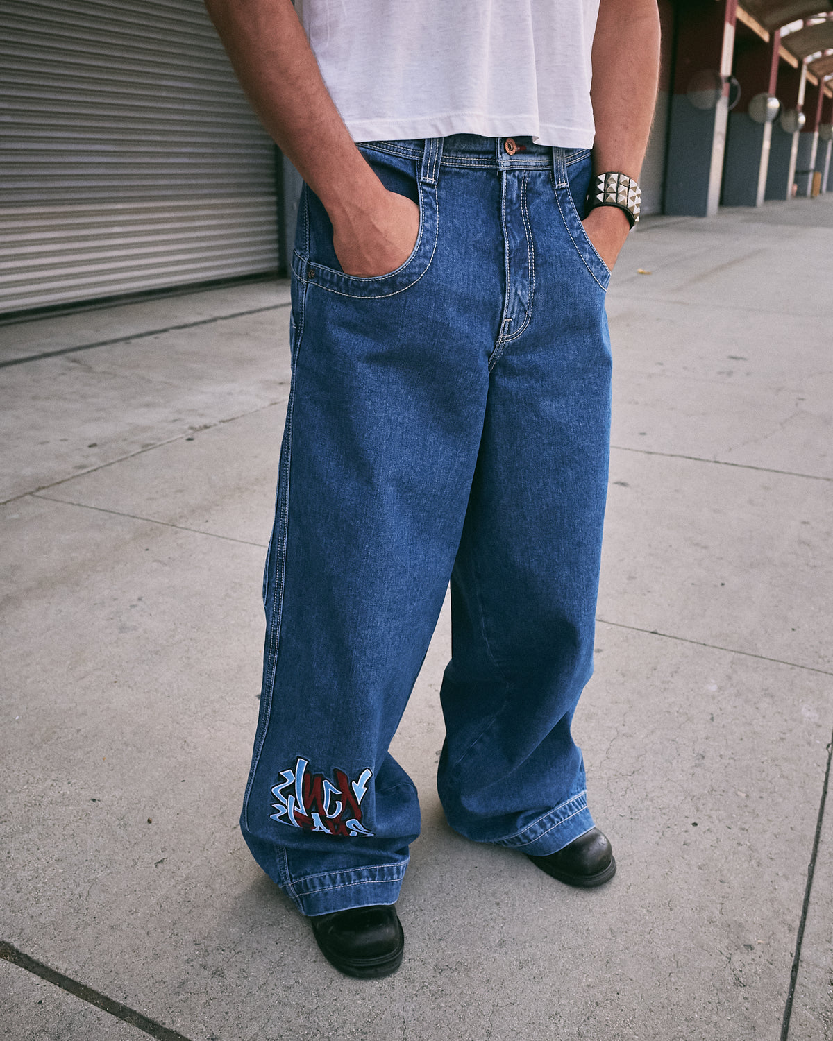 Front view of wide-leg dark stone wash jeans on a model, with red and blue graffiti embroidery on the lower leg