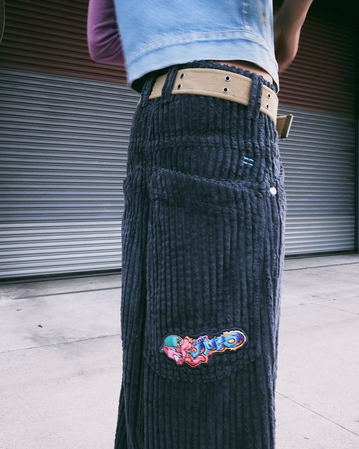 Close-up of the back pocket on dark grey corduroy pants, showing a colorful embroidered cartoon patch