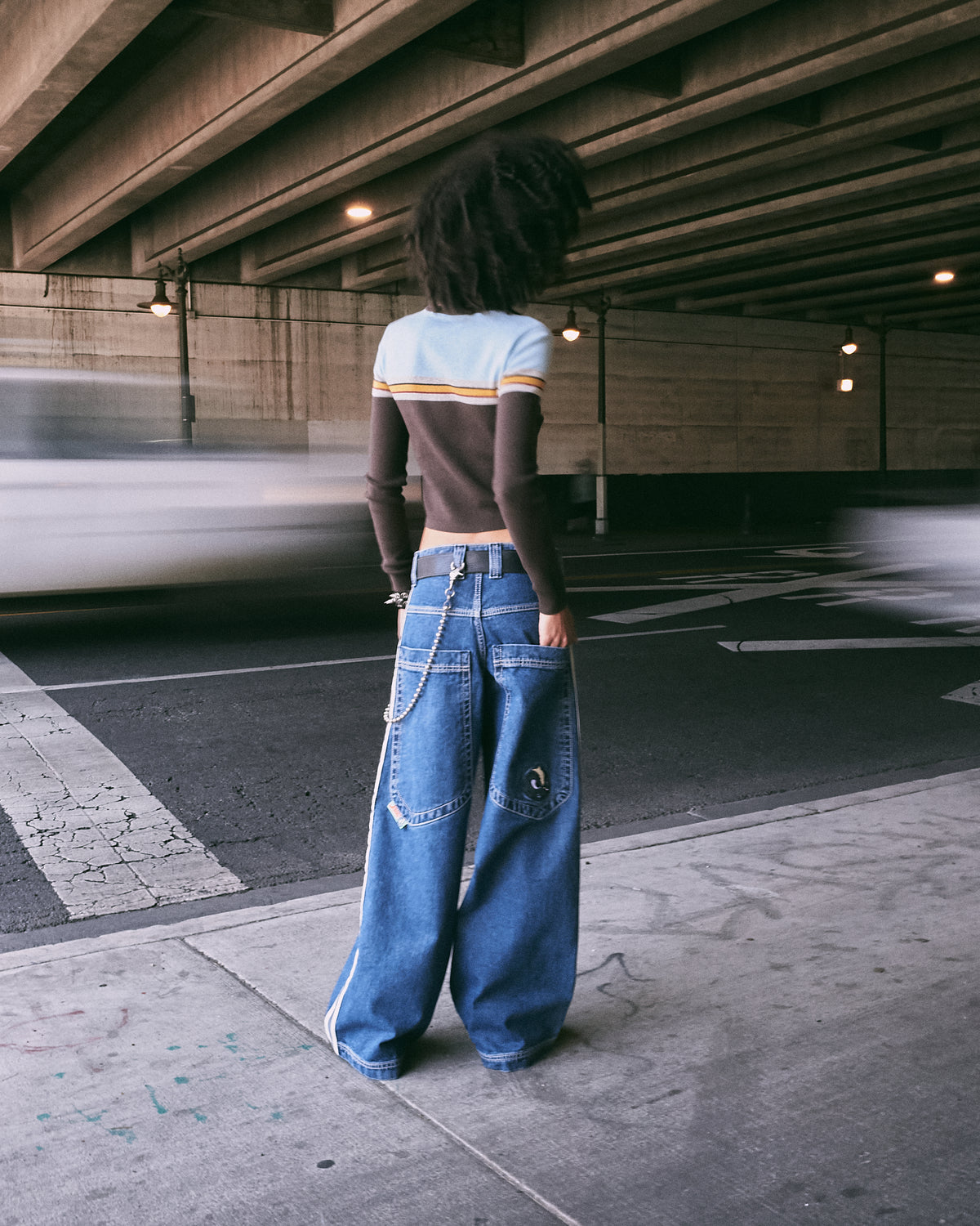 Model wearing dark stone wide-leg jeans, back view showing large back pockets, skunk embroidery and wallet chain