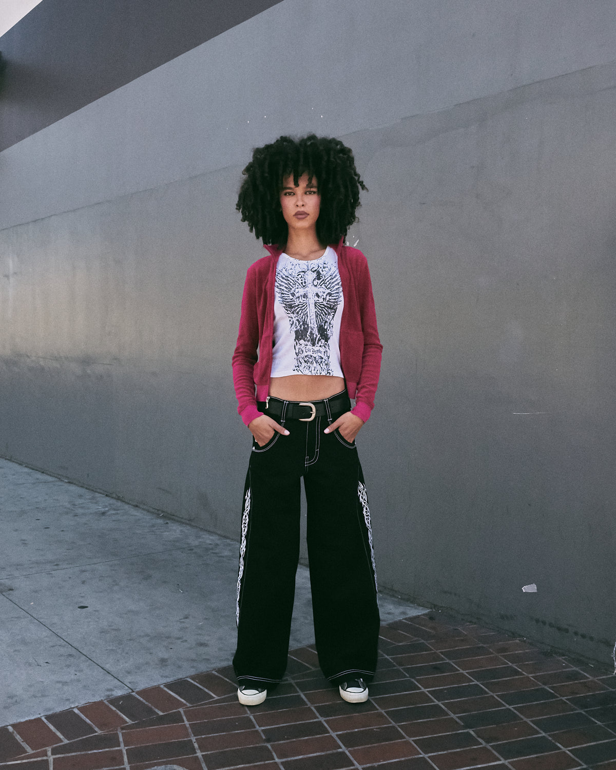 Model standing facing forward in black wide-leg jeans with a belt and white tribal side embroidery