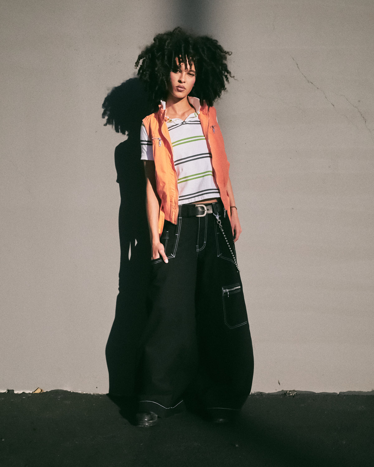 Model wearing wide-leg black jeans with contrast stitching, a belt and wallet chain, full front view