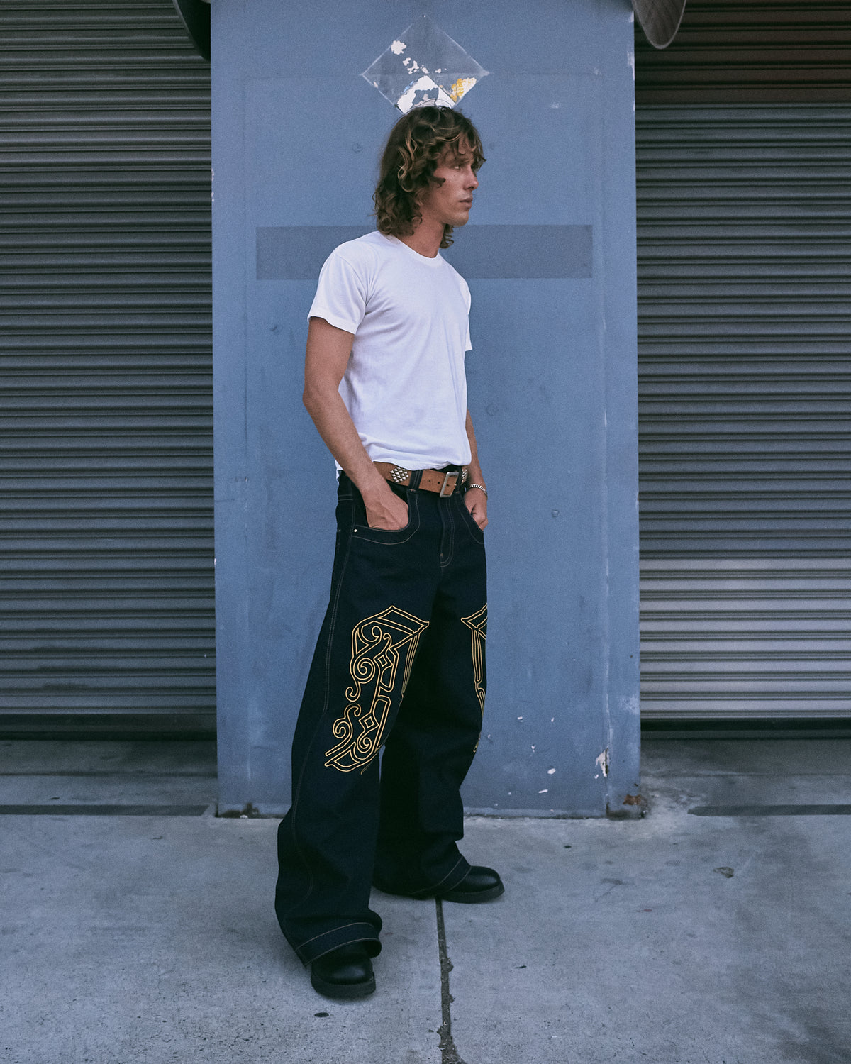 Model in a white T-shirt wearing the dark indigo wide-leg jeans with large gold J embroidery on the thighs, side view