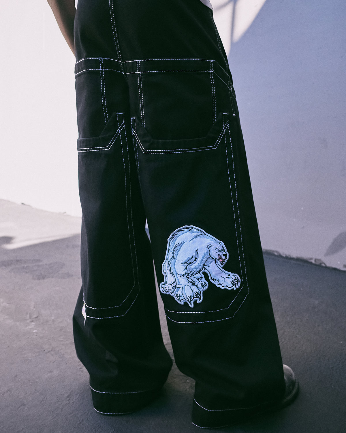Model wearing black wide-leg jeans, back view of the legs showing oversized lower pockets and the polar bear patch