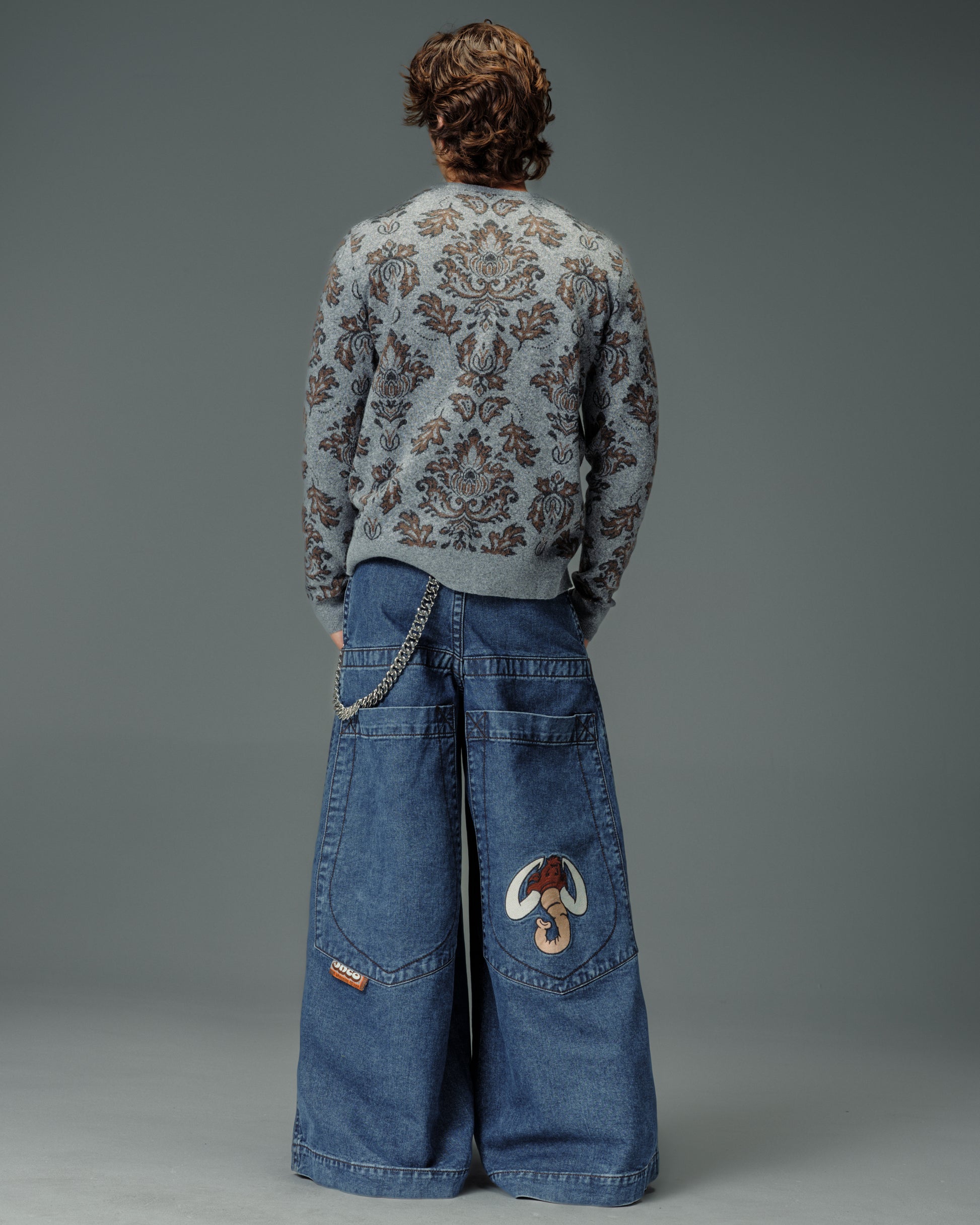 Rear view of a model wearing super-wide embroidered JNCO jeans with a wallet chain