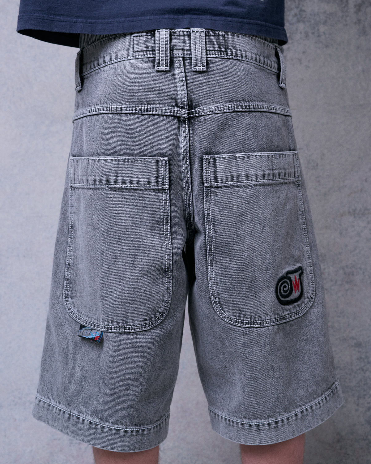 Model wearing faded black denim shorts, back view showing two large back pockets and swirl J embroidery
