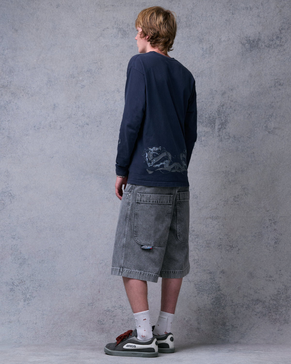 Model wearing knee-length washed black denim shorts, back view showing wide double back pockets