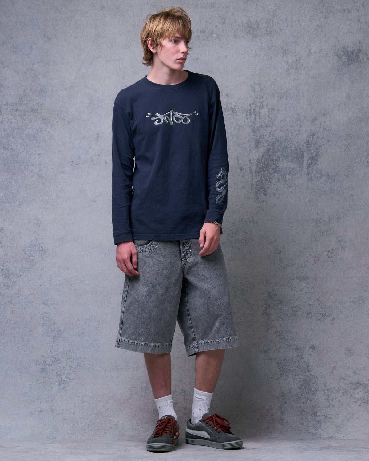 Model wearing washed black denim shorts below the knee, front view with a navy long-sleeve top
