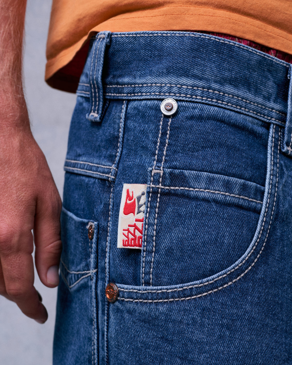Close-up of the front pocket and coin pocket with a woven red crown tag, metal button and copper rivets