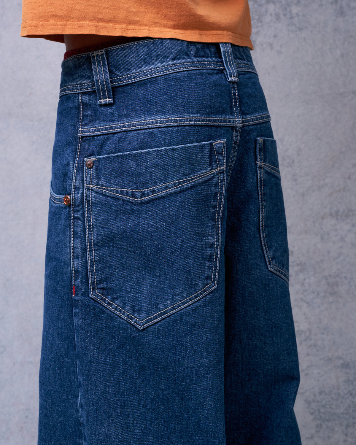 Side-back view of dark stone wash jeans on a model, showing a pointed back pocket and contrast stitching