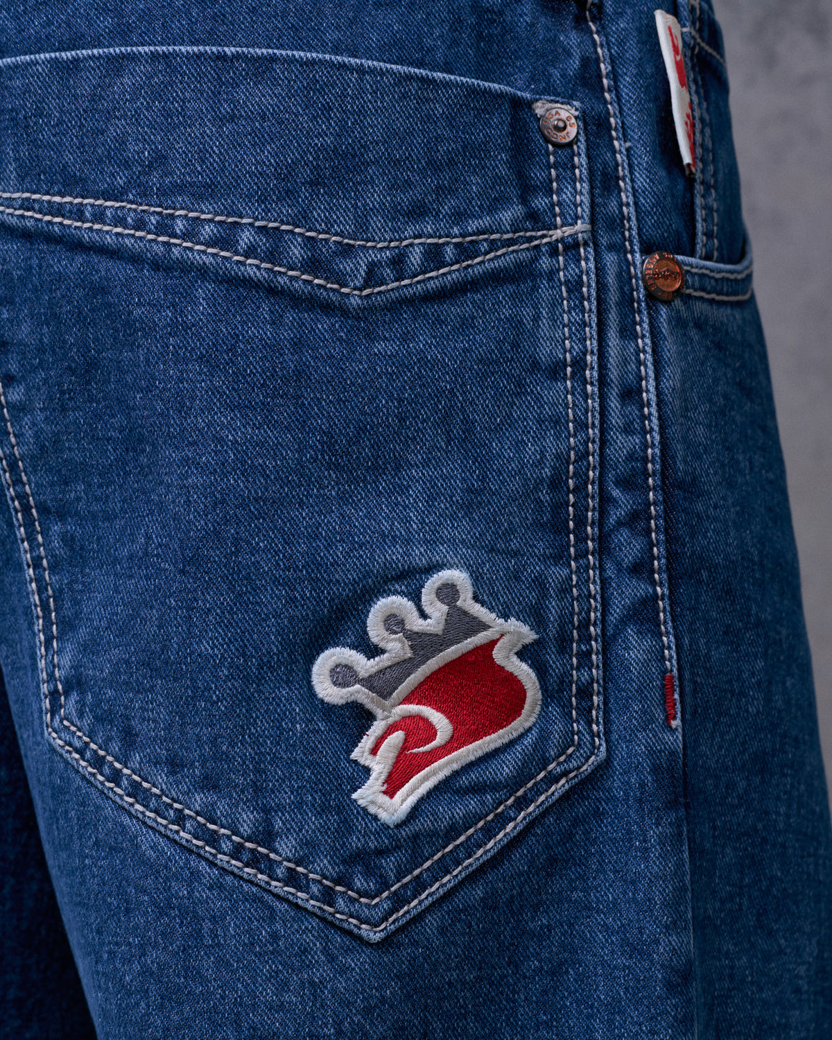 Close-up of the back pocket's red and grey crown embroidery with white outline, copper rivets and contrast stitching