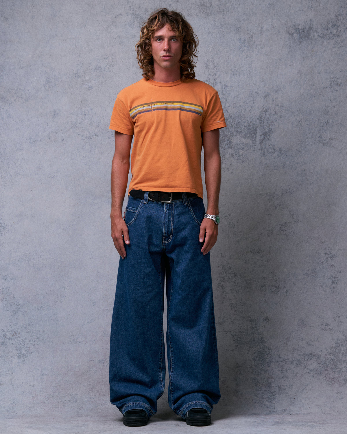 Model wearing dark stone wash wide-leg jeans with a black belt and orange tee, front view