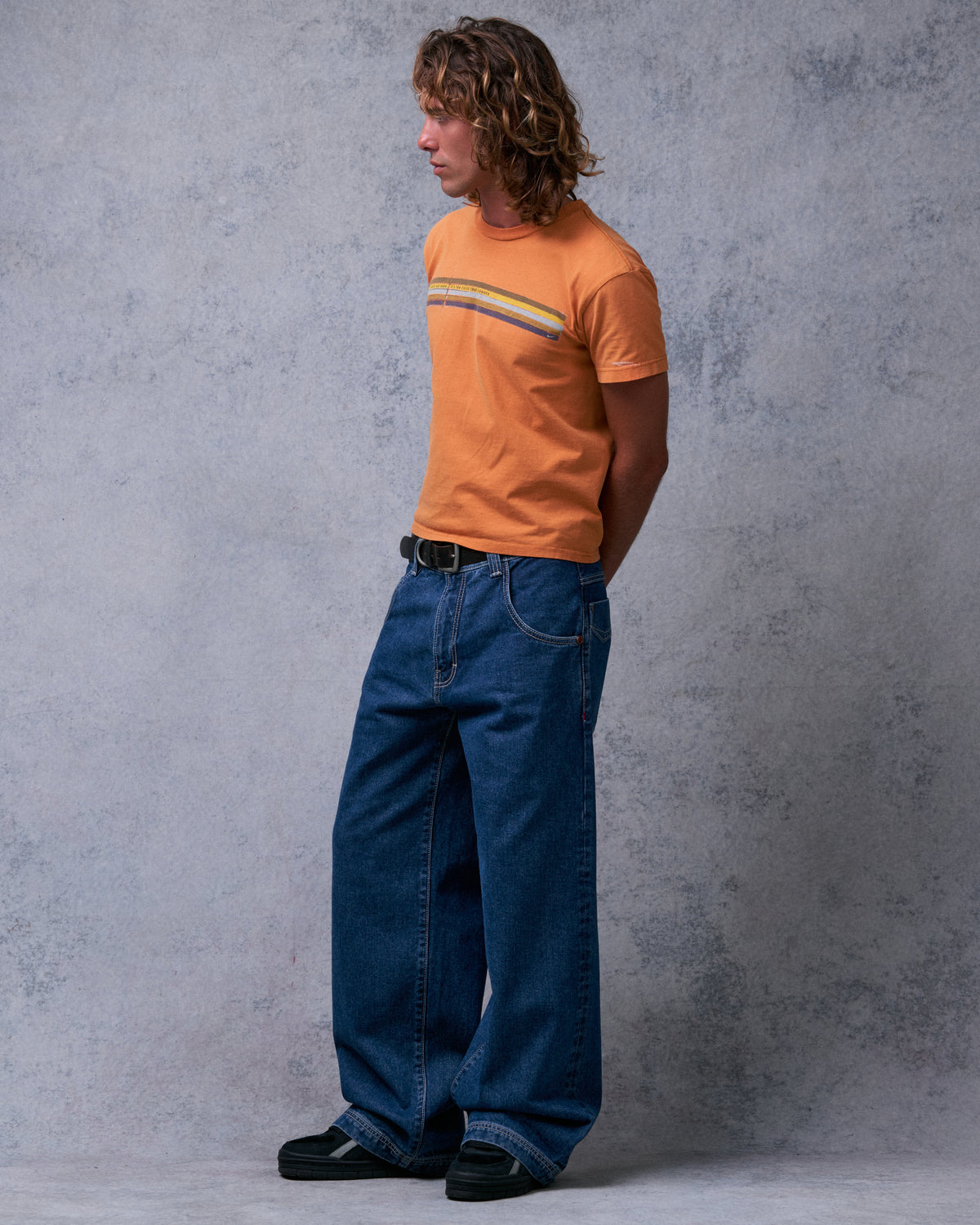 Model wearing dark stone wash wide-leg jeans with hands behind their back, angled side view