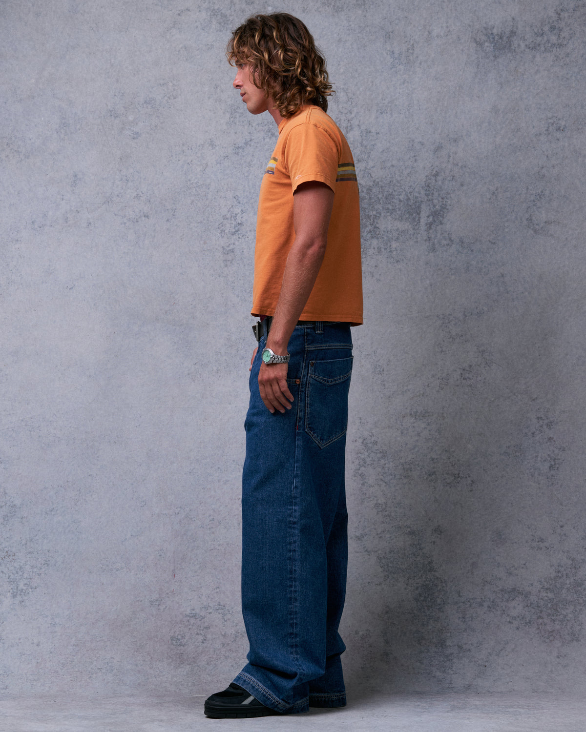 Model wearing dark stone wash wide-leg jeans, side profile showing the full leg width and back pocket