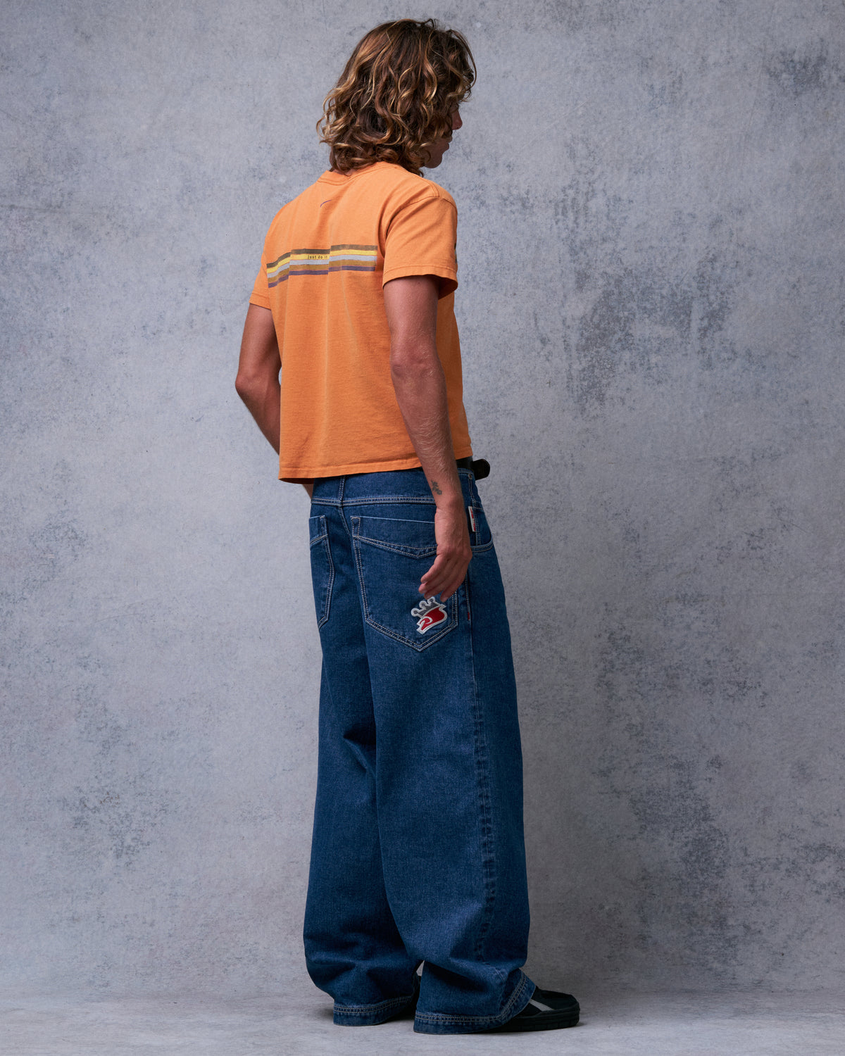 Model wearing dark stone wash wide-leg jeans, back view showing the embroidered crown patch on a back pocket
