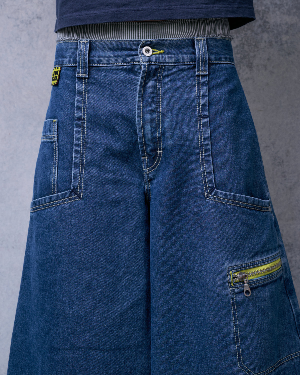 Close-up of the jeans worn from the front, showing the button fly, patch pockets and yellow-taped zip pocket