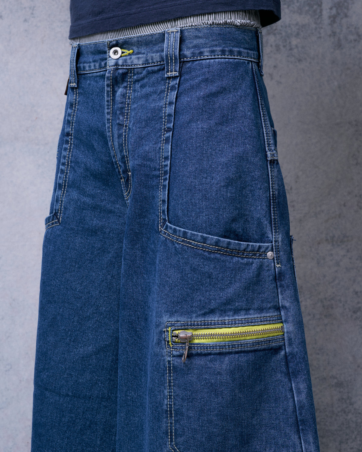 Angled close-up of the jeans worn, focusing on the side patch pocket and yellow zipper tape pocket