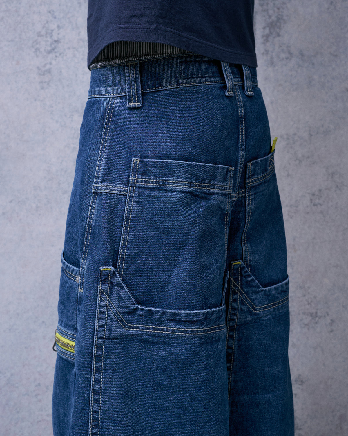 Model wearing the dark stone jeans, angled back view of the deep layered back pockets and a yellow side zipper