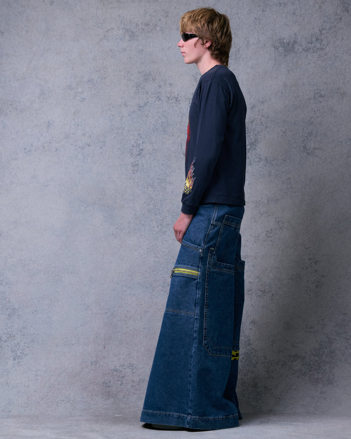 Model wearing the dark stone jeans, side profile showing the 50-inch leg width and yellow-taped zip pocket
