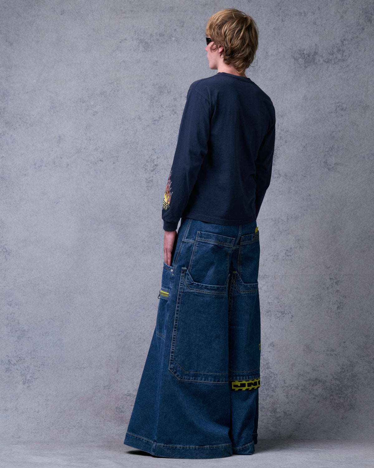 Model wearing the dark stone jeans, rear side view of the back pockets, zip pocket and yellow JNCO tag