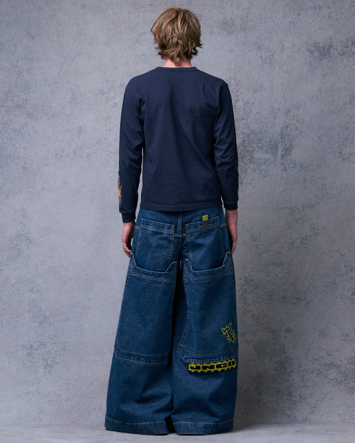 Model wearing the dark stone jeans, straight back view showing long back pockets, yellow Crime Scene embroidery and JNCO tag