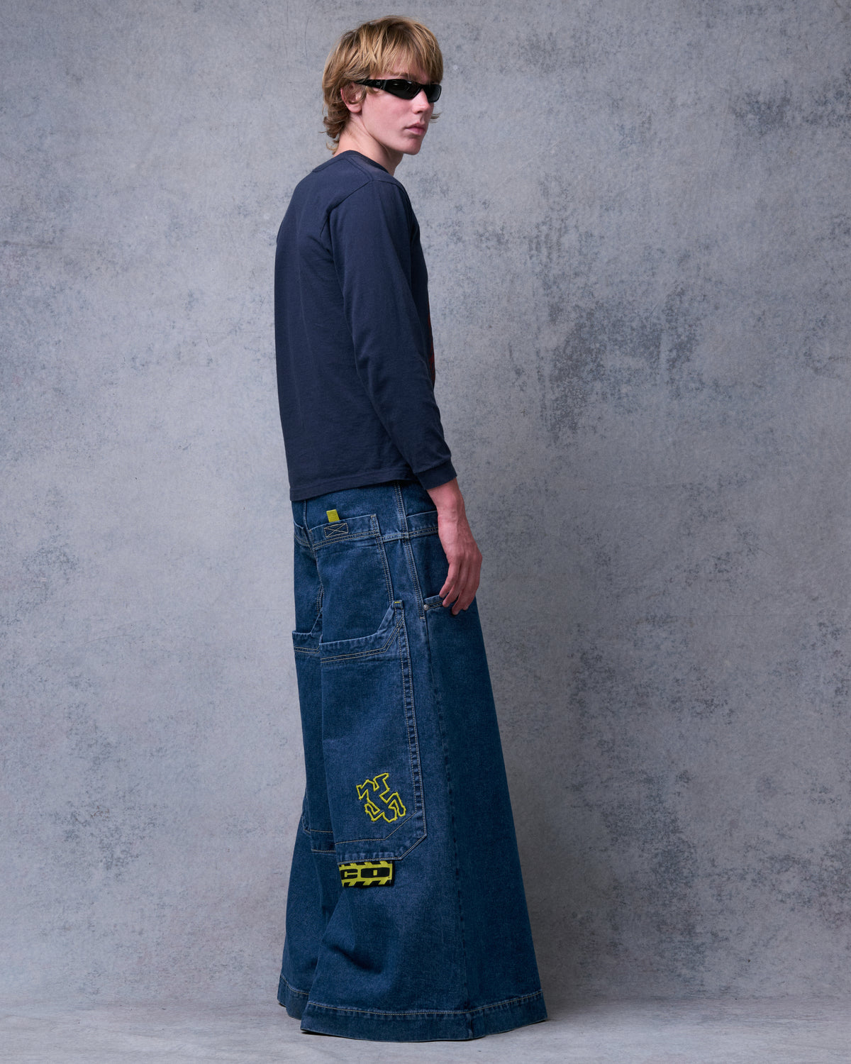 Model wearing the wide-leg dark stone jeans, back three-quarter view showing yellow embroidery and tag on a back pocket