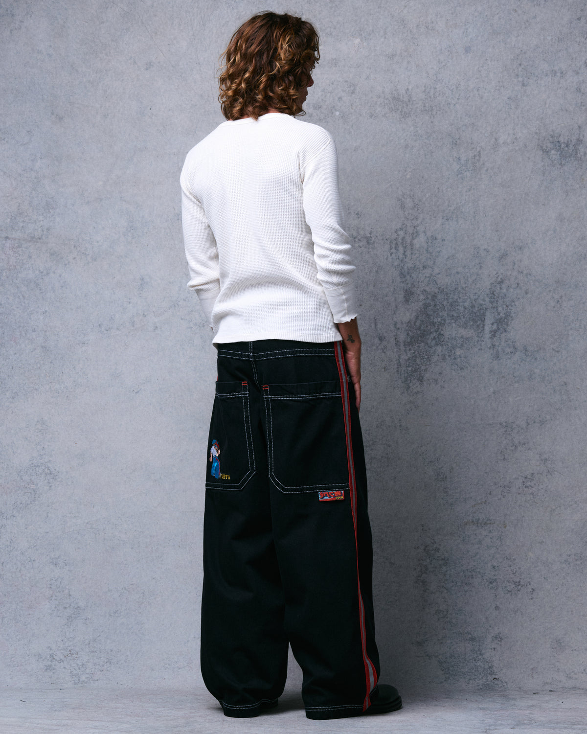 Model wearing wide-leg black jeans, three-quarter back view showing pockets and the side stripe