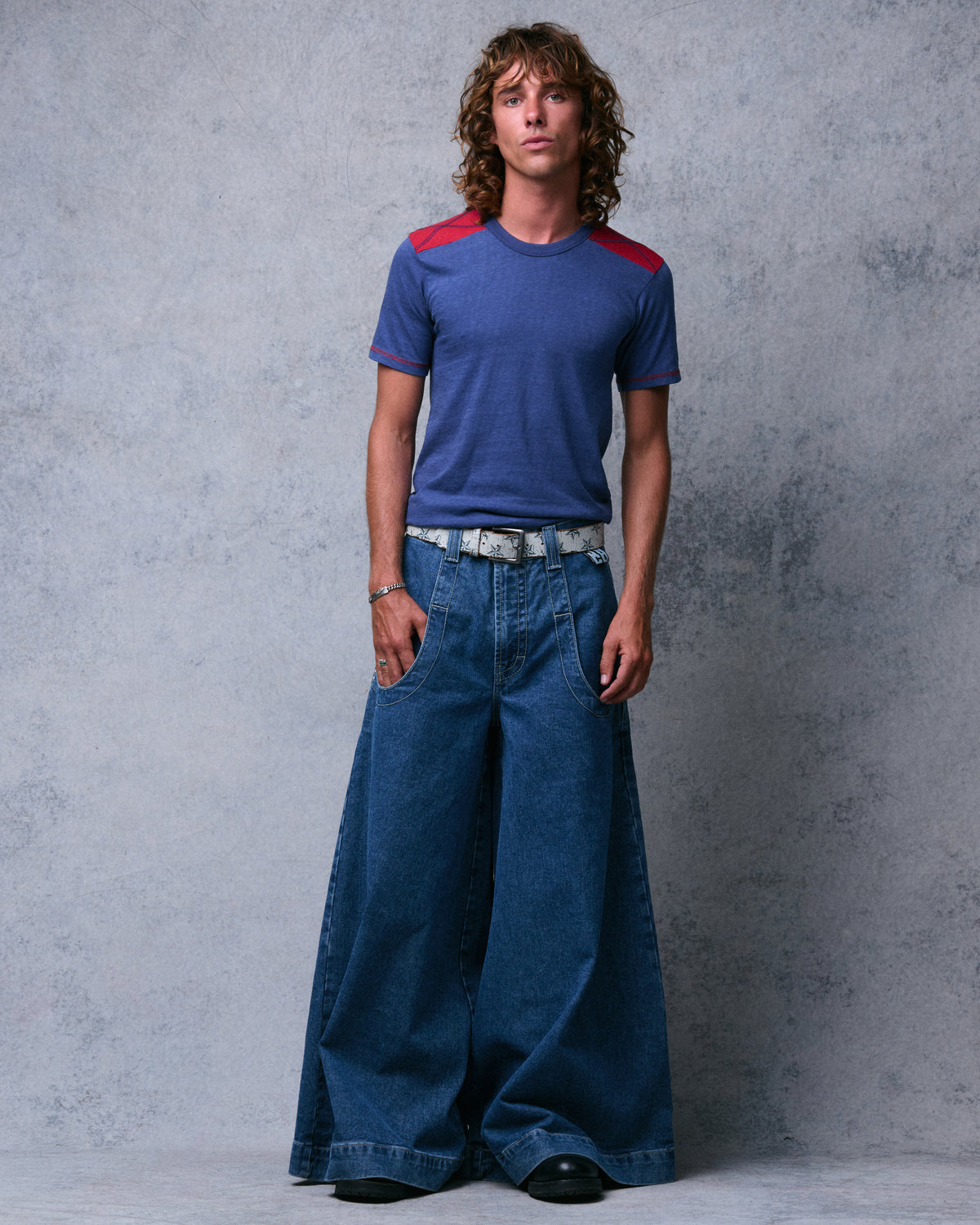 Model wearing dark stone wash extra-wide-leg jeans with a star-print belt, front view, hand in pocket