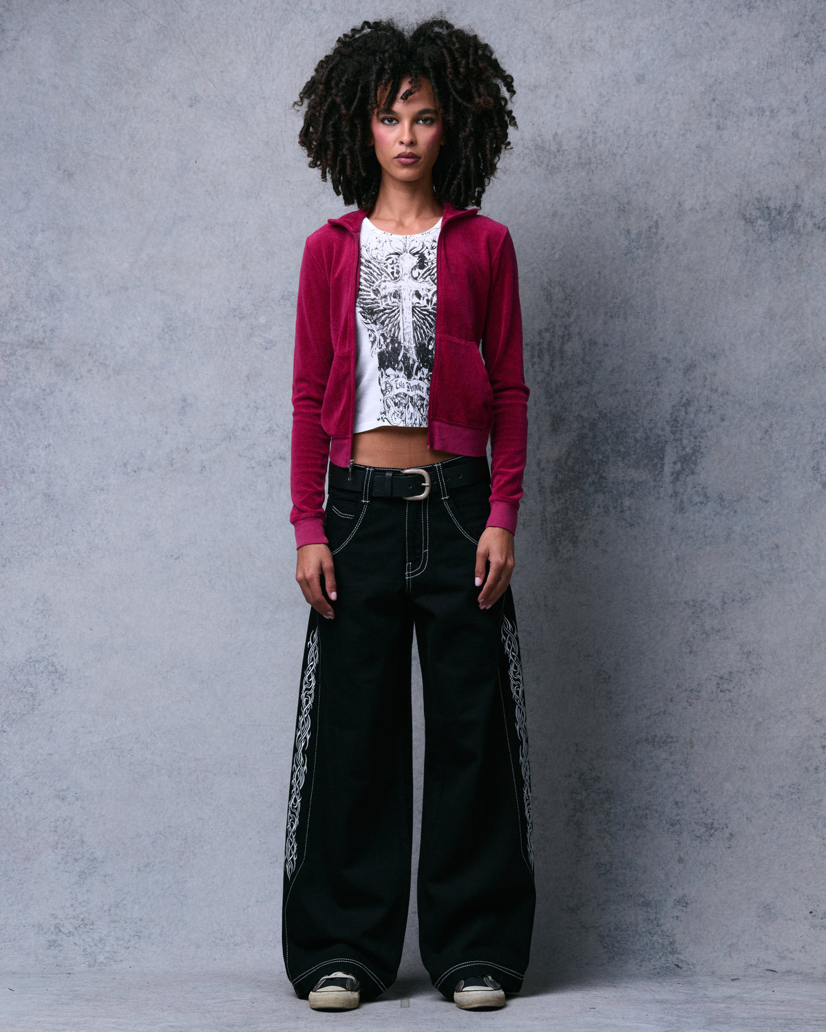 Model wearing black wide-leg jeans with white contrast stitching and tribal embroidery down the sides, front view