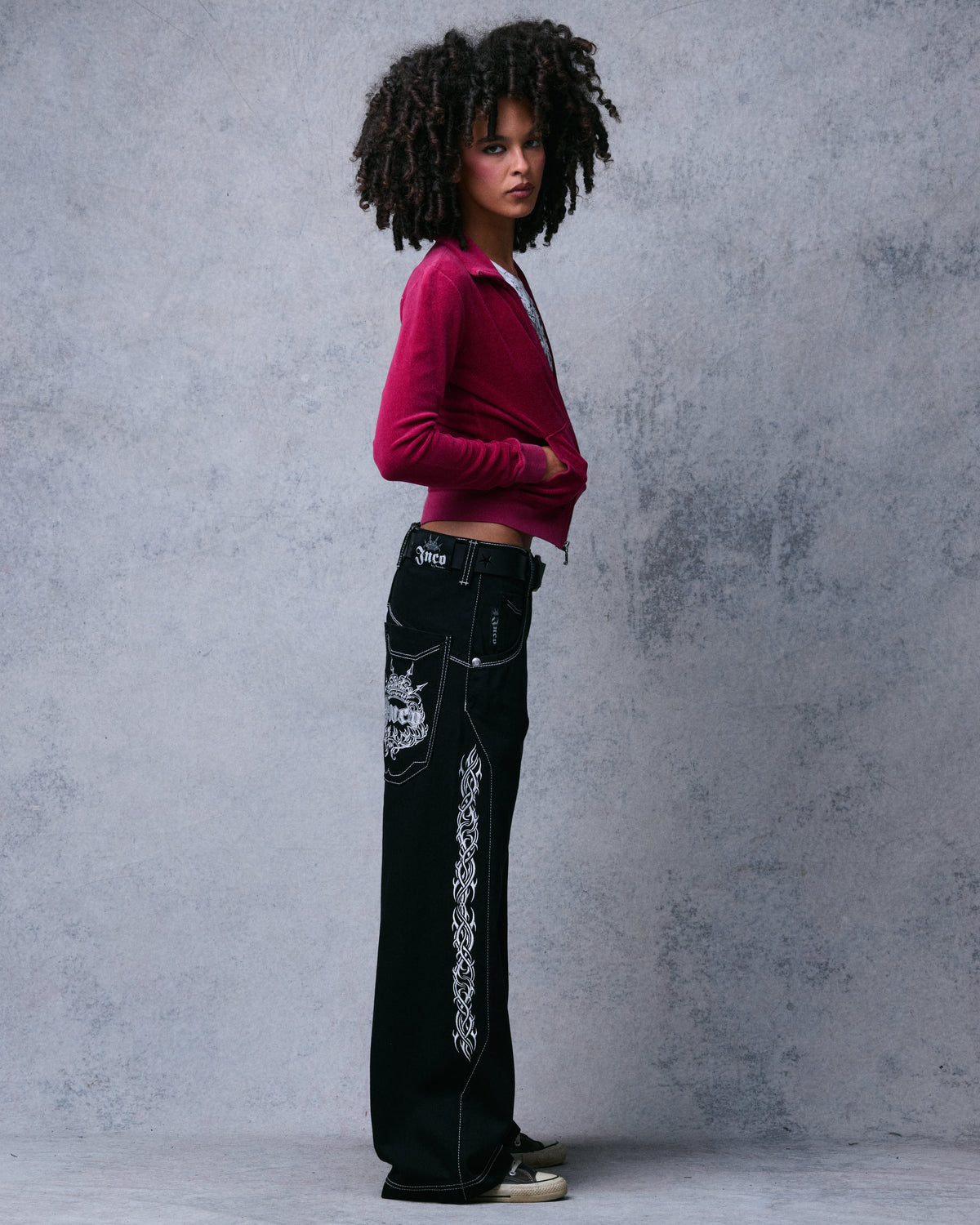 Side profile of the black wide-leg jeans showing tribal side embroidery, crown pocket logo and JNCO waistband patch