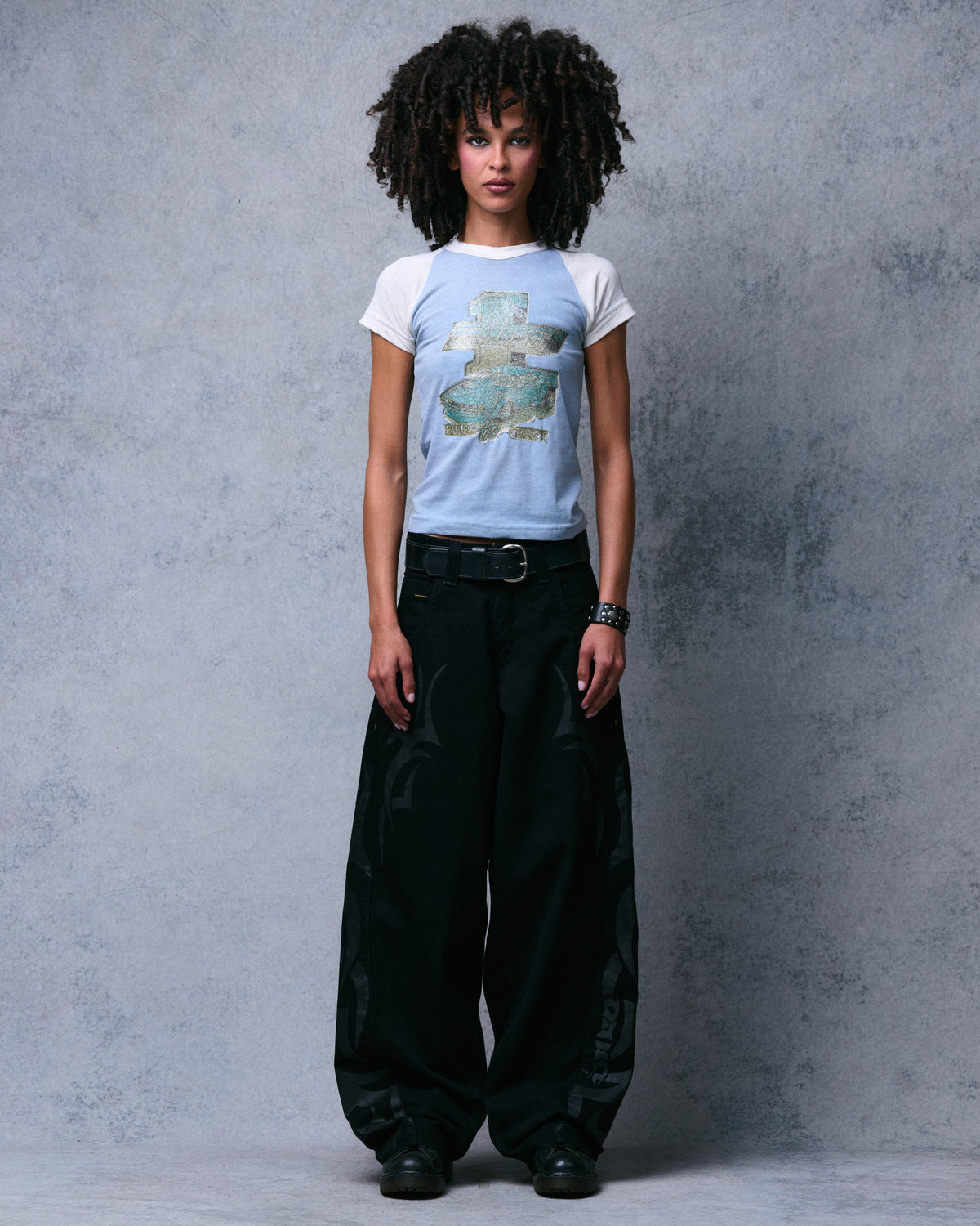 Model wearing wide-leg black jeans with tonal black tribal prints down the legs, front view