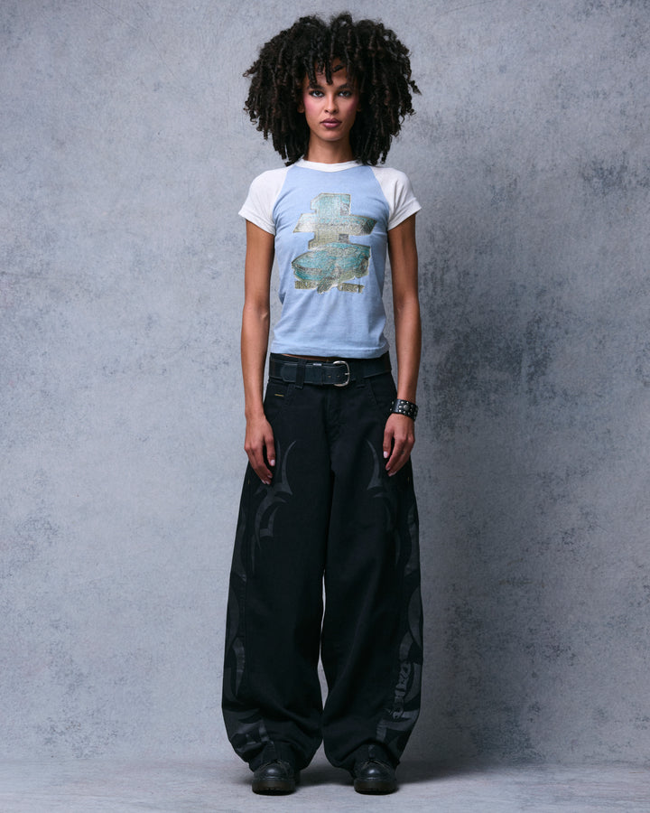 Model wearing the black wide-leg jeans with gray tribal print, a belt and black boots, full-length front view