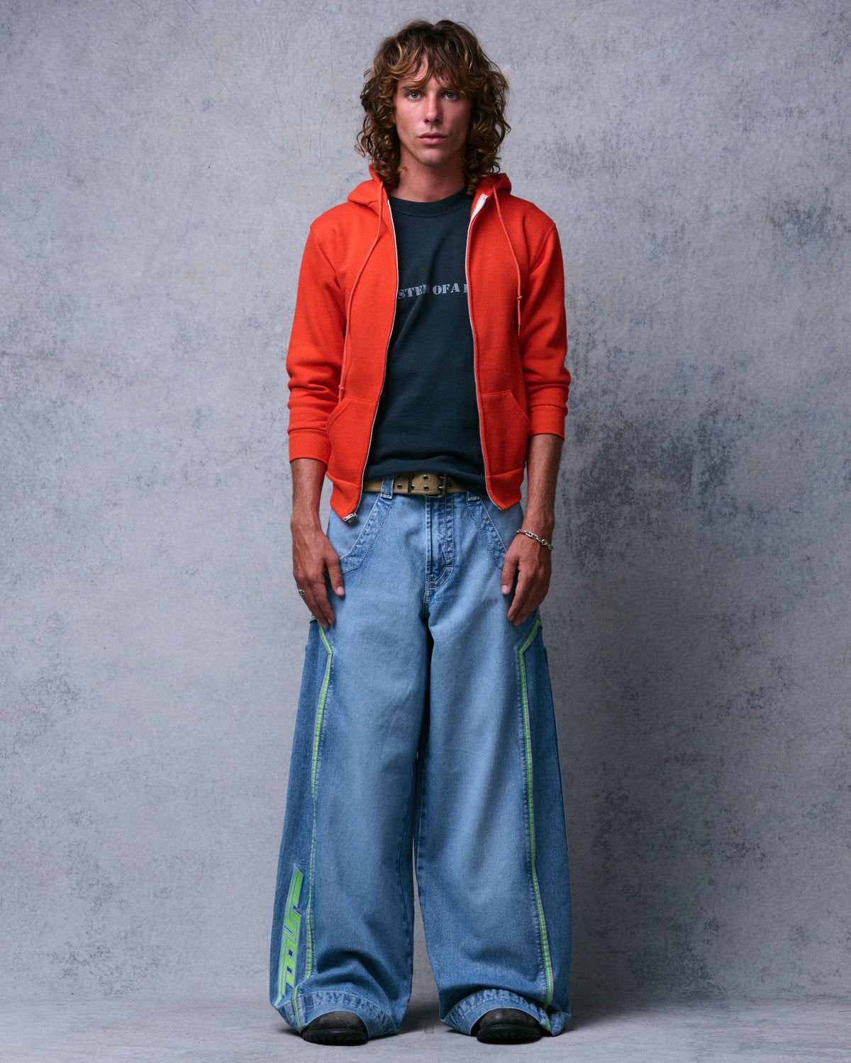 Model wearing the light-wash wide-leg jeans with an orange zip hoodie, full-length front view showing green piping