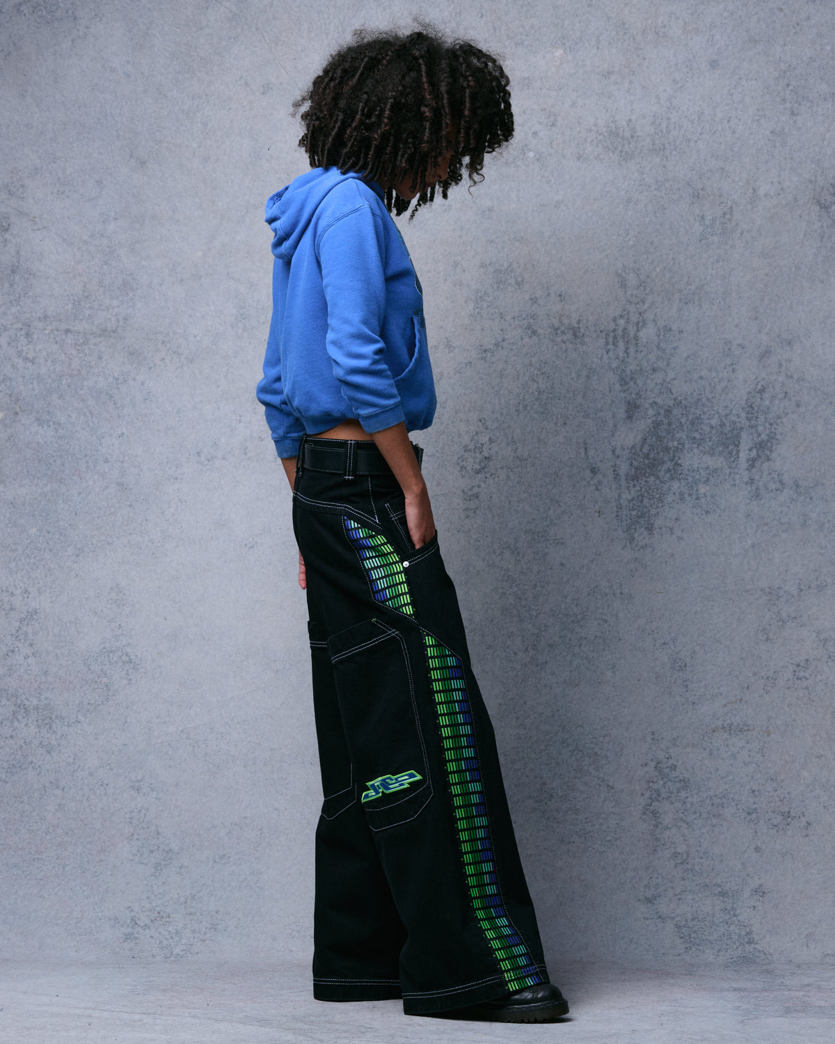Side profile of the black wide-leg jeans showing the full green and blue equalizer-bar panel and embroidered back pocket