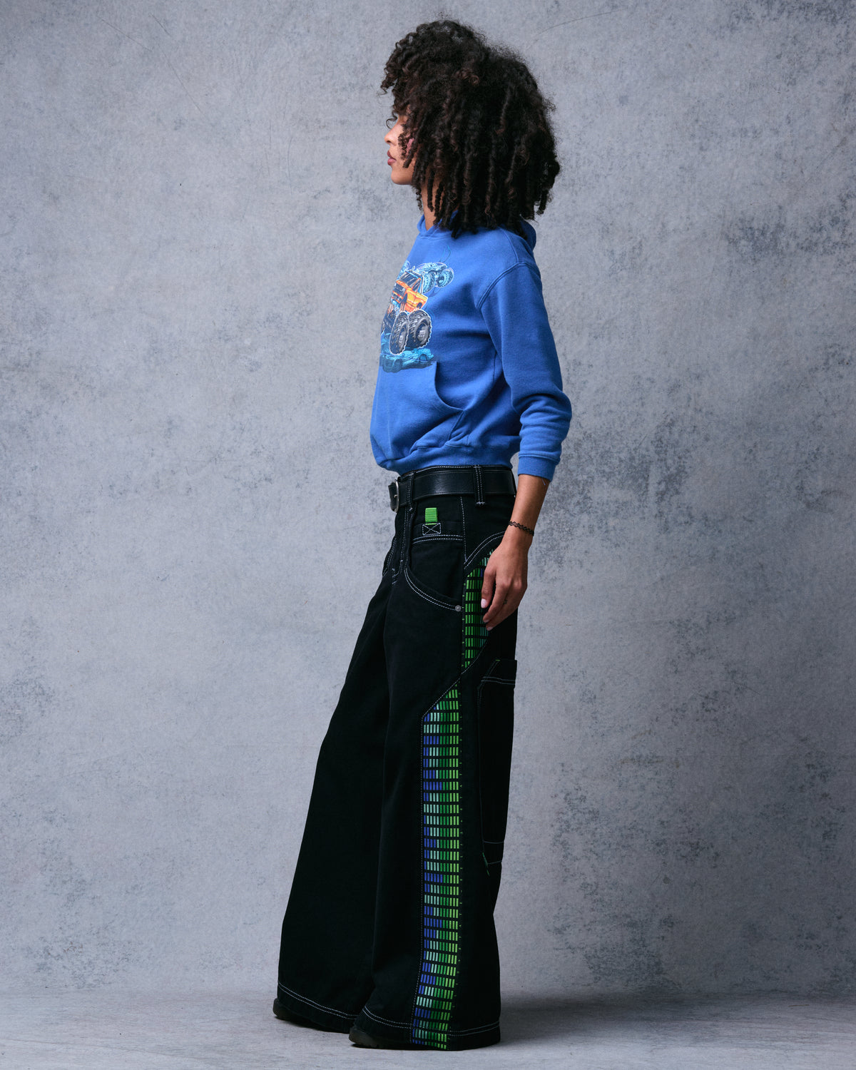Model wearing black wide-leg jeans with green and blue equalizer-pattern side panels, side view