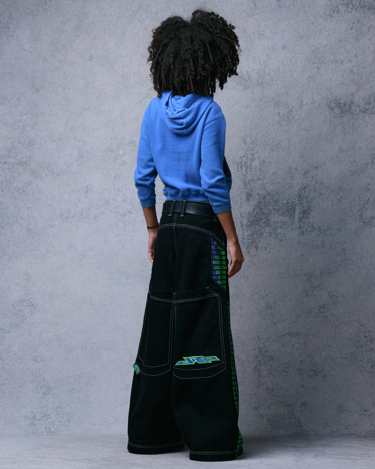 Model wearing black wide-leg jeans, back view showing large back pockets and green JNCO embroidery